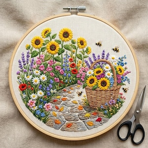 May include: A circular embroidery hoop containing a fabric panel with a detailed needlepoint scene of a stone path, a woven basket filled with sunflowers and daisies, surrounded by lavender, poppies, and bees, with black metal scissors nearby.