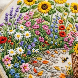 May include: A circular embroidery hoop featuring a vibrant garden scene with yellow sunflowers, purple lavender, white daisies, red poppies, and pink wildflowers. A small embroidered bee is positioned near a woven basket and stone path.