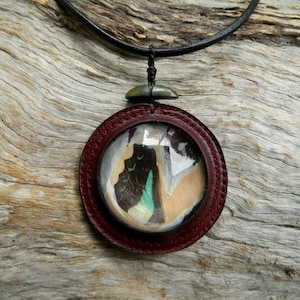 May include: A round leather pendant necklace with a red leather frame and a clear glass dome containing a colorful butterfly wing. The necklace is on a black leather cord.