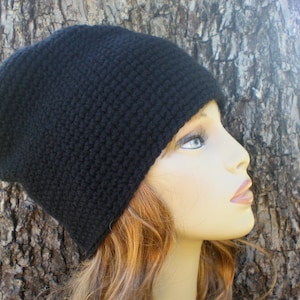 May include: A black knitted beanie hat. The hat is made of a textured, dark yarn and has a simple, classic design. The hat is shown on a mannequin head with light skin and blonde hair.