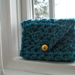 May include: A teal blue crocheted clutch purse with a gold button closure.
