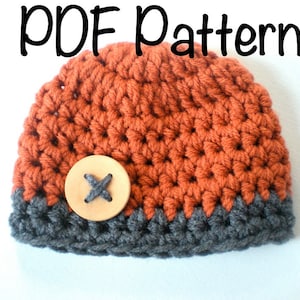 Puede incluir: Un gorro de punto con un botón en naranja y gris. El gorro tiene un texto superpuesto "PDF Pattern".