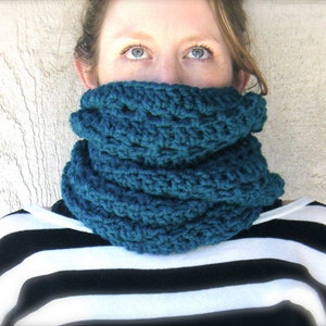 May include: A teal blue crocheted cowl neck scarf. The scarf is thick and warm, perfect for cold weather.