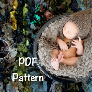 May include: A newborn baby wearing a brown knitted hat is sleeping in a brown fluffy basket. The basket is sitting on a bed of colourful shredded fabric.