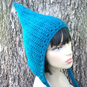 May include: A teal blue crocheted hat with a pointed crown and long ties. The hat is worn on a mannequin head.