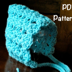 May include: A light blue crocheted baby bonnet with a lacy pattern. The bonnet has a long tie that can be tied under the chin. PDF Pattern.