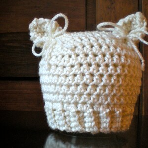 May include: White crocheted baby hat with two ear flaps tied with white yarn.
