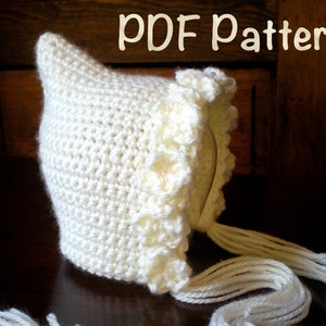 Könnte beinhalten: Eine weiße Häkelmütze für Babys mit einem gekräuselten Rand und langen weißen Garnbändern. Die Mütze ist ein PDF-Muster.