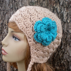 May include: A crocheted hat with a large turquoise flower on the side. The hat is beige and has a long tie.