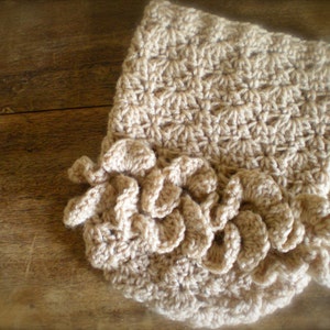 Peut inclure: Un chauffe-cou crocheté beige avec un bord festonné.