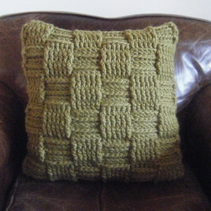 May include: A green knitted cushion with a woven pattern sits on a brown leather sofa.