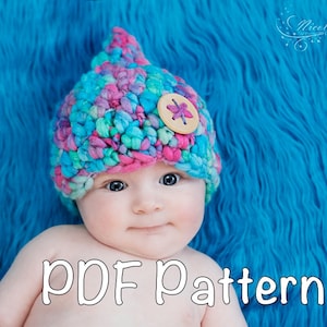 May include: A baby wearing a colorful crocheted hat with a flower button on top. The hat is pink, blue, green, and purple. The baby is lying on a blue fuzzy blanket. The text "PDF Pattern" is written in white on the bottom of the image.