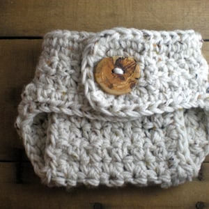 Puede incluir: Una cubierta de pañal para bebé de crochet blanco con un botón de madera. La cubierta de pañal está hecha con un hilo texturizado y tiene un diseño simple.