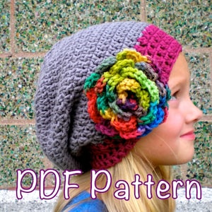 May include: A crochet hat with a large, colorful flower on the side. The hat is gray and pink, and the flower is made of multiple colors of yarn. The hat is being worn by a young person with long blonde hair. The text "PDF Pattern" is visible at the bottom of the image.