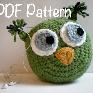 May include: Green crocheted owl with white and blue eyes, a yellow beak, and black yarn for the eyebrows. The owl is wearing headphones.