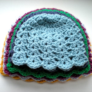 May include: A stack of crocheted hats in various colors, including yellow, purple, green, blue, and light blue. The hats are layered on top of each other, with the light blue hat on top.