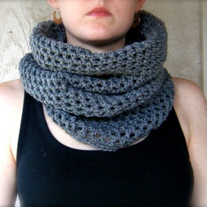 Peut inclure: Une écharpe en crochet infinie grise avec un motif texturé. L'écharpe est portée par une personne avec un débardeur noir.