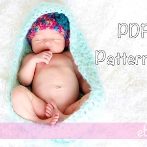 Op de afbeelding: PDF-patroon voor een gehaakte baby muts en deken. De muts is roze, blauw en groen. De deken is lichtblauw. De baby slaapt in de deken.