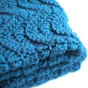 May include: A teal blue crocheted blanket with a textured, woven pattern.