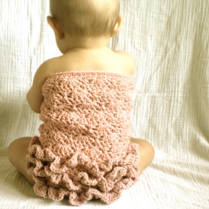 May include: A baby wearing a pink crocheted dress with a ruffled hem.