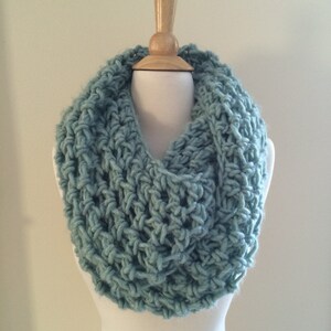 May include: A light blue crocheted infinity scarf. The scarf is made with a chunky yarn and has a loose, open weave.