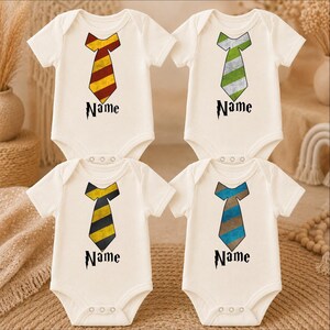 May include: Four cream-colored short-sleeve baby bodysuits, each featuring a graphic of a necktie in different color combinations: red and yellow, green and white, yellow and black, and blue and brown. Below each tie is the word Name in black.