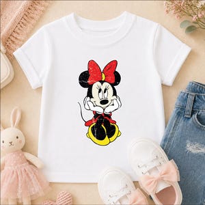 A white t-shirt with a Minnie Mouse graphic, a pair of white sneakers, and a pair of blue jeans are arranged on a surface.