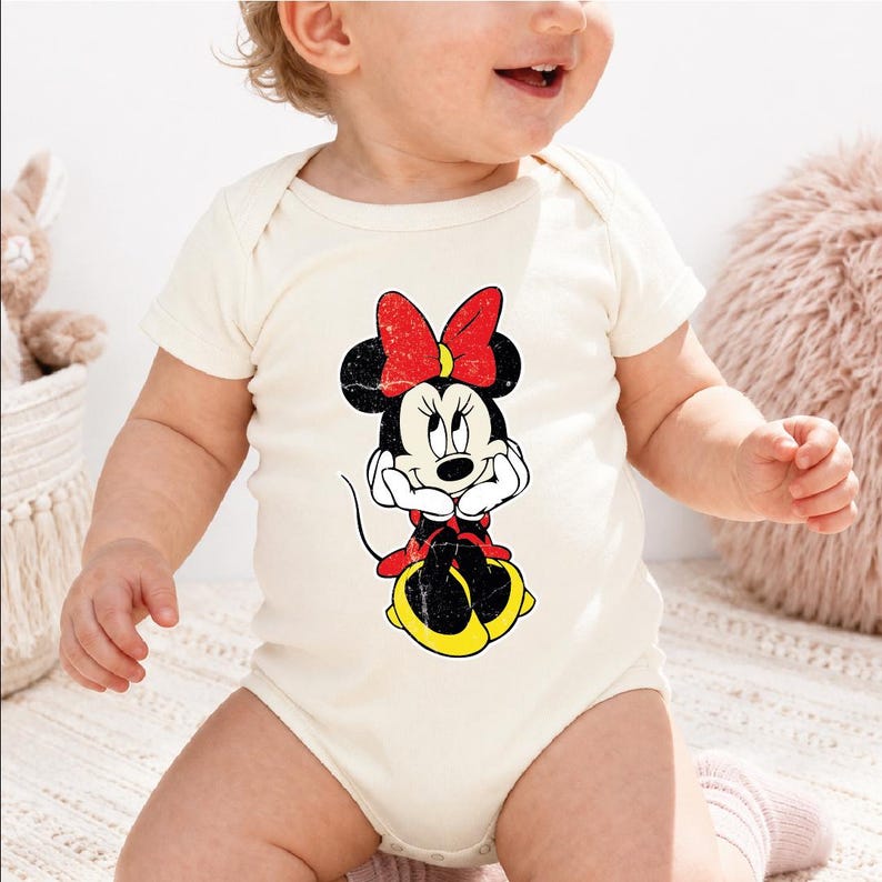 A baby wearing a white onesie with a Minnie Mouse graphic on it.