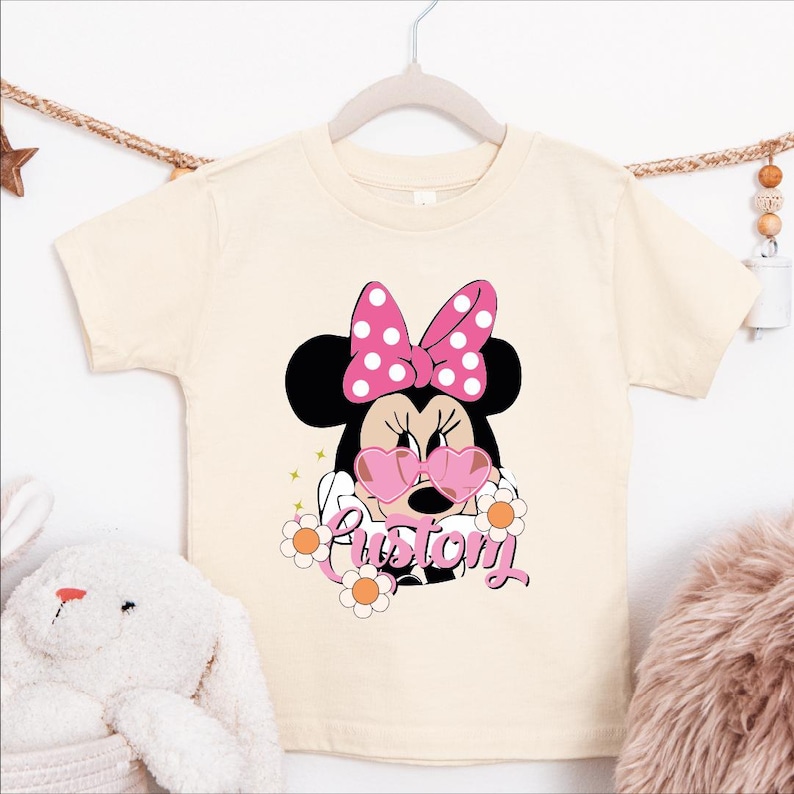 A white t-shirt with a Minnie Mouse design and the word "Custom" printed on it, hanging on a clothing hanger.