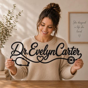 May include: A black wall sign featuring the name Dr. Evelyn Carter in a cursive script font. The design incorporates a stethoscope graphic that forms a heart shape in the center and extends to the name, creating a continuous medical-themed line.