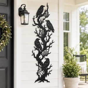 May include: A tall, vertical black wall decoration featuring a detailed tree branch design with four perched ravens and intricate spider webs woven between the branches. The piece is crafted with a textured finish and mounted on a white wall.
