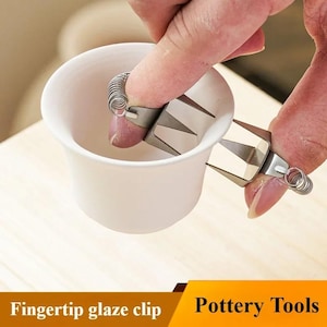 Peut inclure: Une pince à glaçure pour le bout des doigts en acier inoxydable tient une tasse en céramique blanche. La pince a un ressort et des dents angulaires. Le texte "Fingertip glaze clip" et "Pottery Tools" est au bas de l'image.