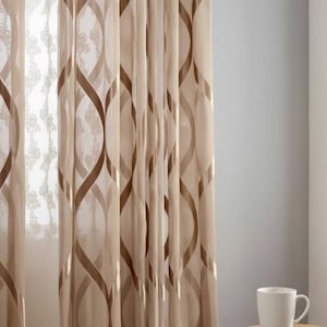 May include: Sheer beige curtains with a repeating brown, curved pattern. The curtains are hanging in front of a window, and a white mug sits on a table in the foreground. The curtains are made of a lightweight fabric.