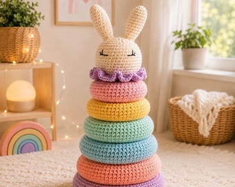 May include: A crochet stacking toy featuring a cream-colored rabbit head topper with embroidered eyes, followed by a ruffled purple collar and six stacked rings in pastel shades of pink, yellow, mint green, light blue, peach, and lavender.