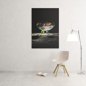 May include: A rectangular wall art print featuring a surreal scene of two figures sitting on a cratered lunar surface, looking out at a large, glowing Earth suspended in a dark black sky. The composition emphasizes the contrast between the dark space.