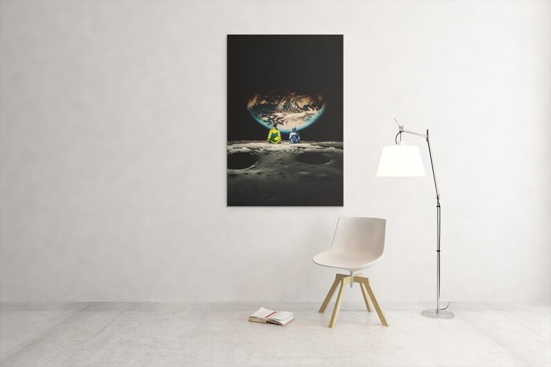 May include: A rectangular wall art print featuring a surreal scene of two figures sitting on a cratered lunar surface, looking out at a large, glowing Earth suspended in a dark black sky. The composition emphasizes the contrast between the dark space.