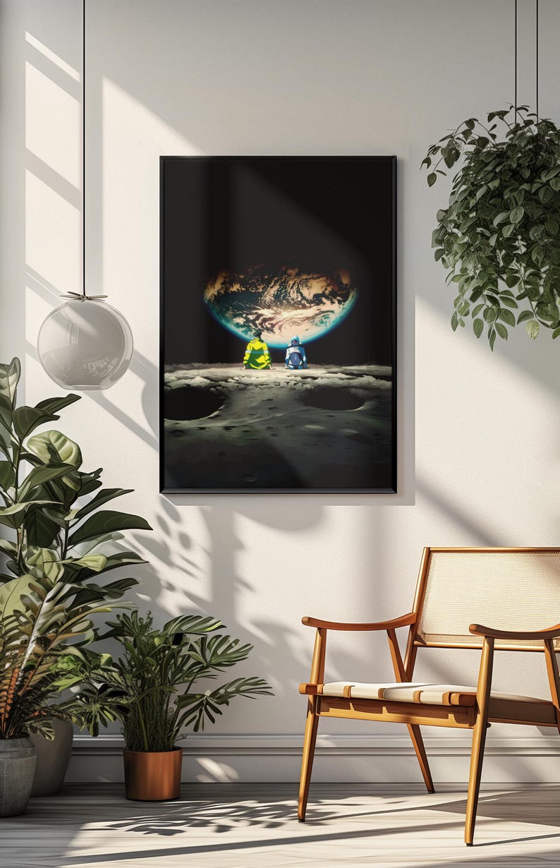 May include: A rectangular wall art print in a black frame featuring a dark space scene. Two figures sit on a cratered lunar surface, looking toward a glowing, illuminated Earth suspended in the black void of space above the horizon line.