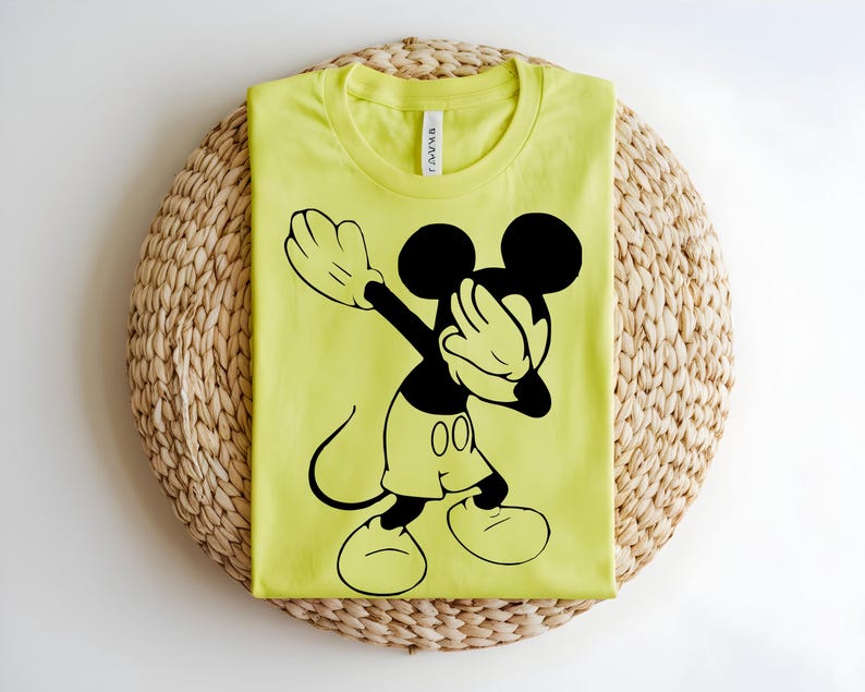 K&ouml;nnte beinhalten: Ein leuchtend neongelbes T-Shirt mit Rundhalsausschnitt und einem gro&szlig;en schwarzen Grafikdruck von Mickey Mouse in einer Dab-Pose. Das T-Shirt hat ein klassisches Kurzarm-Design mit einem sichtbaren wei&szlig;en Markenetikett im Kragenbereich.