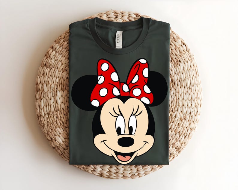 Puede incluir: Una camiseta de cuello redondo gris oscuro con un gr&aacute;fico de Minnie Mouse. El personaje tiene la cabeza negra, orejas grandes y redondas y un lazo rojo brillante con lunares blancos. El dise&ntilde;o est&aacute; centrado en el pecho de la camiseta.