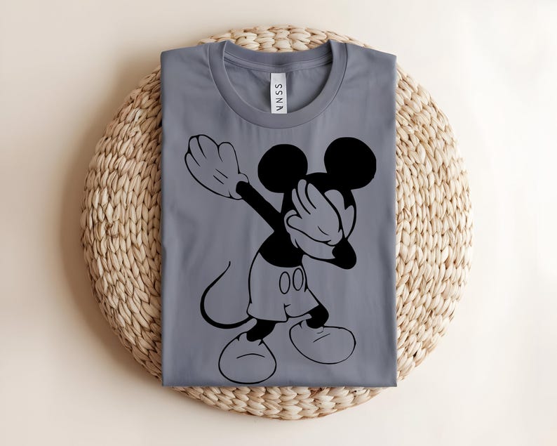 K&ouml;nnte beinhalten: Ein graues Kurzarm-T-Shirt mit einem schwarzen Grafikdruck einer Zeichentrick-Mausfigur, die eine Dabbing-Pose ausf&uuml;hrt. Das T-Shirt hat einen Rundhalsausschnitt und ein wei&szlig;es Innenetikett am Nacken mit dem Text SSNA in schwarzer Schrift.