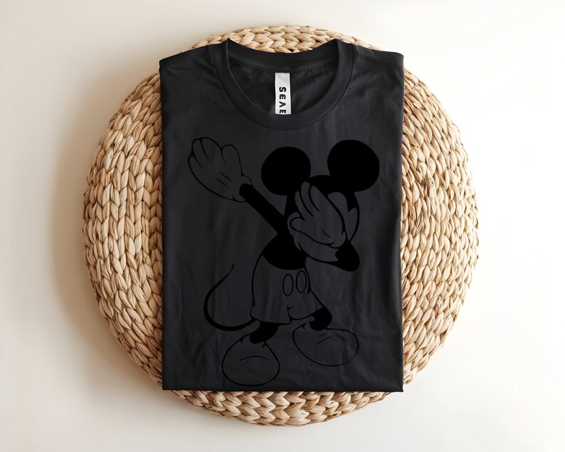K&ouml;nnte beinhalten: Ein schwarzes Kurzarm-T-Shirt mit einer schwarzen grafischen Umrisszeichnung der Figur Mickey Mouse, die eine Dab-Tanzbewegung ausf&uuml;hrt. Das Shirt hat einen Rundhalsausschnitt und ein wei&szlig;es Markenetikett am inneren Kragenbereich auf dem dunklen Stoff.