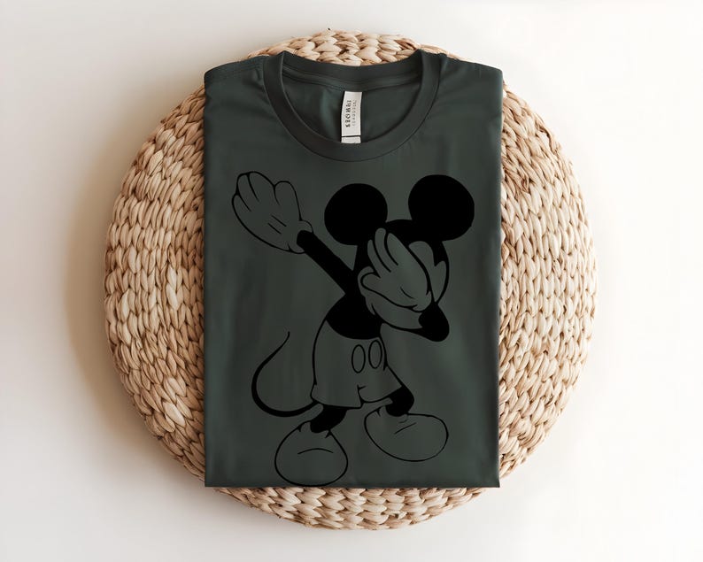 K&ouml;nnte beinhalten: Ein dunkel anthrazitfarbenes T-Shirt mit Rundhalsausschnitt und einem schwarzen Grafikdruck der Zeichentrickfigur Mickey Mouse, die eine Dab-Pose ausf&uuml;hrt. Das Shirt hat einen klassischen Kurzarm-Schnitt und ein sichtbares Markenetikett am Kragen.
