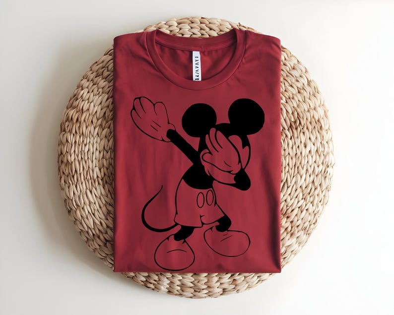 K&ouml;nnte beinhalten: Ein dunkelrotes T-Shirt mit Rundhalsausschnitt und einem schwarzen Grafikdruck von Mickey Mouse, der eine Dab-Pose ausf&uuml;hrt. Das Shirt hat ein wei&szlig;es Nackenetikett mit schwarzem Text am Kragen. Das Motiv ist mittig auf der Vorderseite platziert.