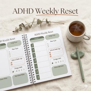 Könnte beinhalten: Ein offener Wochenplaner mit dem Titel "ADHD Weekly Reset" und Spiralbindung. Er enthält Abschnitte für tägliche Aufgaben und Energielevel. Das Design verwendet eine gedämpfte Farbpalette. Eine Tasse Tee und eine Stifthalterung liegen daneben.