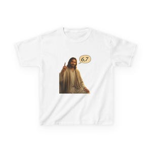 Op de afbeelding: Wit T-shirt met een afbeelding van een persoon met lang haar en een baard, die omhoog wijst. Een tekstballon bevat de cijfers "6,7". De persoon draagt een lichtbruine jurk. Het T-shirt is gemaakt van een zacht, comfortabel materiaal.