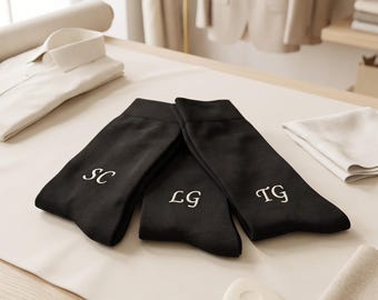 May include: Three black socks laid flat, each featuring a unique white embroidered monogram. The left sock displays the letters SC, the center sock shows LG, and the right sock features the letters TG in a classic serif font style.