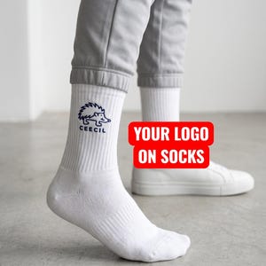 May include: White crew socks featuring a dark blue embroidered hedgehog graphic and the text CEECIL on the outer side. The socks are worn with light gray joggers and white sneakers. A red rectangular graphic with white text reads YOUR LOGO ON SOCKS.