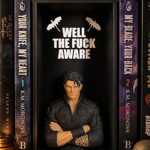 May include: A black book nook insert featuring a male bust with dark hair and a tattoo on the forearm, arms crossed. The back panel displays the white text WELL THE FUCK AWARE beneath two white bat silhouettes, flanked by two books titled Your Knife, My Heart.