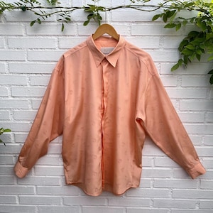 May include: A long-sleeve button-down shirt in a solid peach color featuring a subtle, repeating tonal pattern of small, abstract circular motifs. The shirt has a classic collar, a front button placket, and buttoned cuffs, with a label reading TIPO'S.