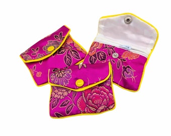 May include: Three small pink fabric pouches with floral patterns and yellow trim. The pouches have a zipper closure and a button closure.